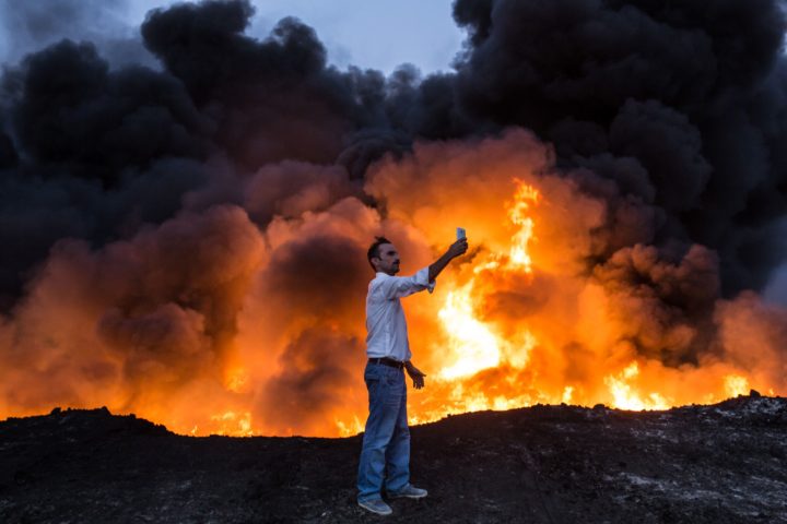 TOPSHOT - A man takes a selfie in front of a fire from oil that has been set ablaze in the Qayyarah area, some 60 kilometres (35 miles) south of Mosul, on October 19, 2016, during an operation by Iraqi forces against Islamic State (IS) group jihadists to retake the main hub city. In the biggest Iraqi military operation in years, forces have retaken dozens of villages, mostly south and east of Mosul, and are planning multiple assaults for October 20. / AFP PHOTO / YASIN AKGUL