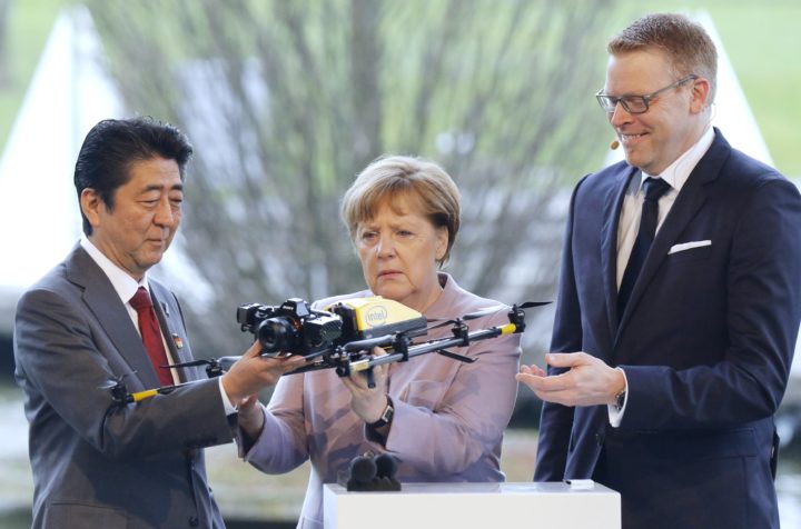 De Duitse bondskanselier Angela Merkel (midden) bekijkt een drone met de Japanse premier Shinzo Abe (R) - Foto: AFP